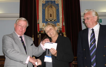 Mrs Joyce Steele receiving the £1000 cheque from Lodge Charity Steward, WBro Tony Norman with Lodge Almoner, WBro John Walsh, looking on